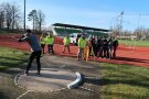 Ein Kugelstoßer, Schülerinnen und Schüler mit Messgeräten im Hintergrund